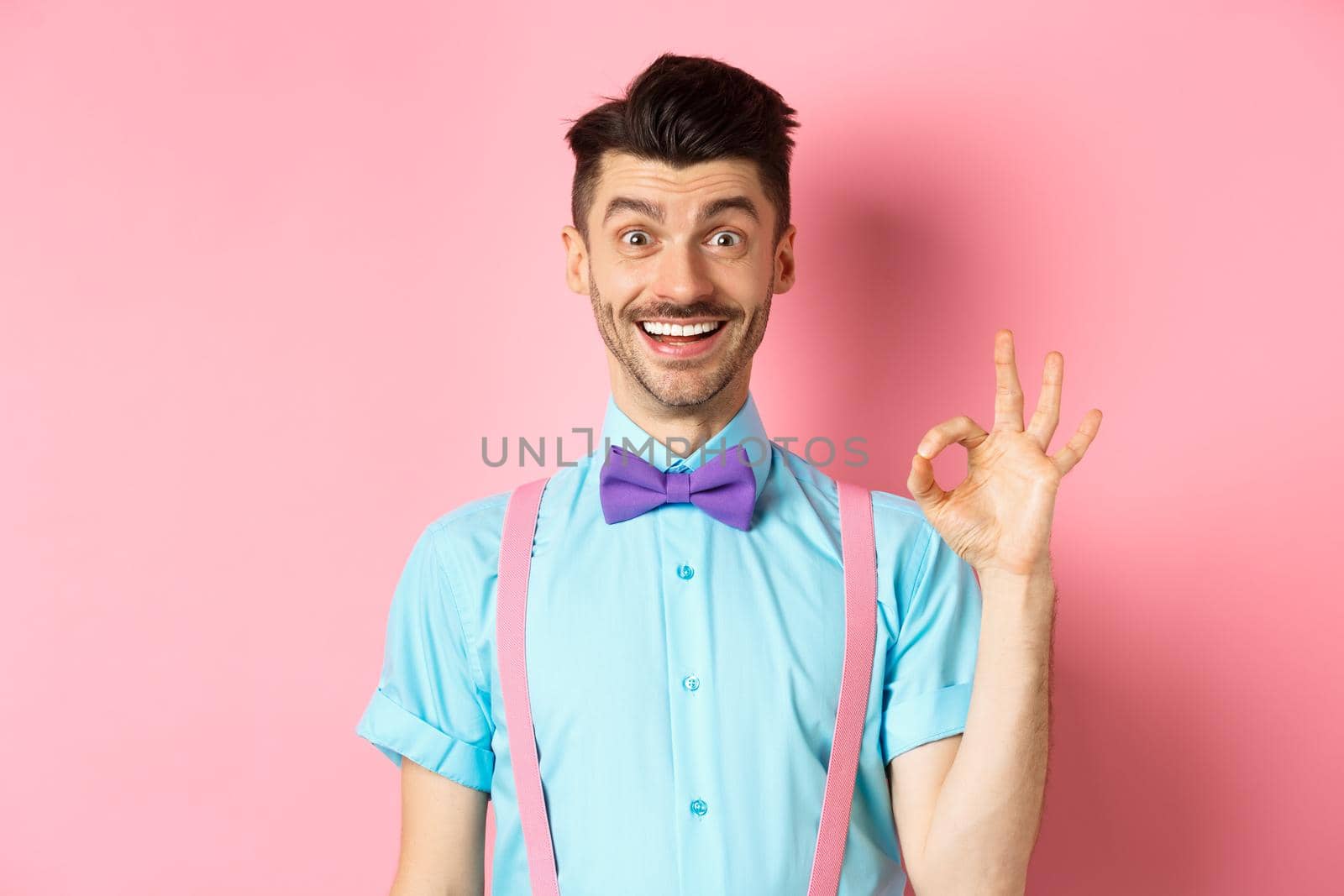 Handsome caucasian man with moustache smiling and showing okay sign, approve something good, praising excellent choice, standing amused on pink background.