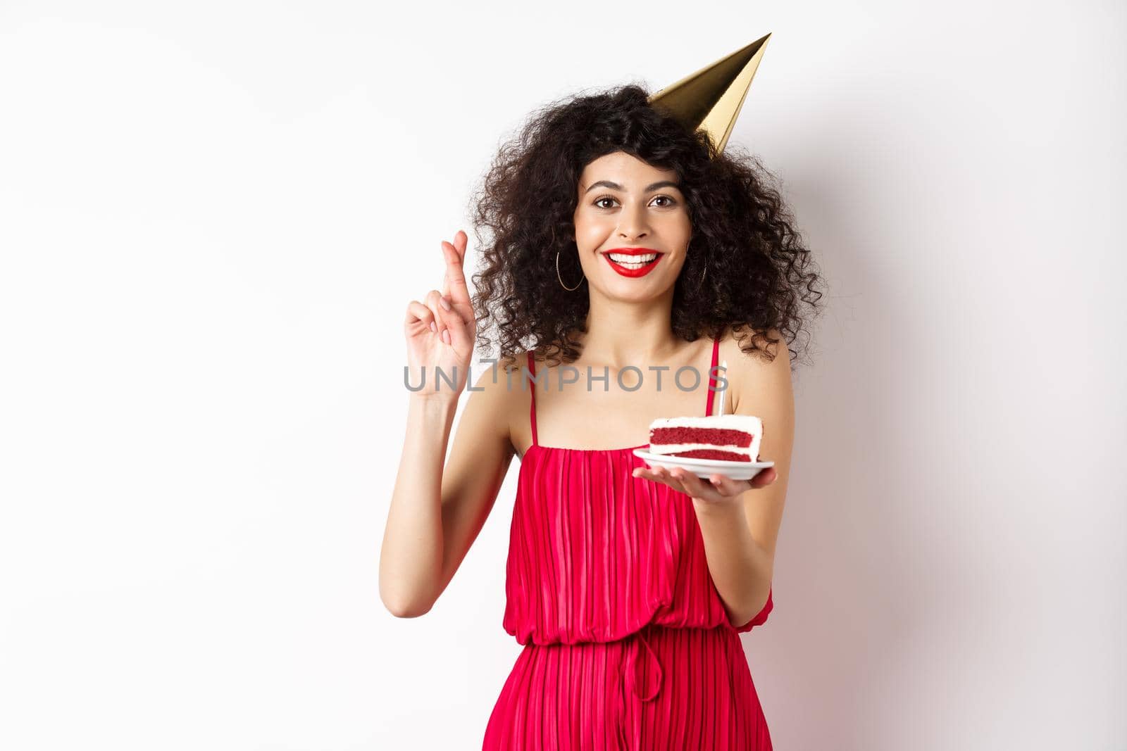 Excited birthday girl celebrating, making wish, holding cake and cross fingers good luck, standing happy on white background.