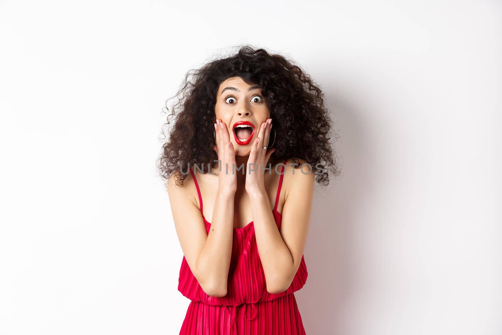 Image of elegant woman scream surprised, staring at camera, see promo offer and shouting of joy, standing in dress over white background by Benzoix