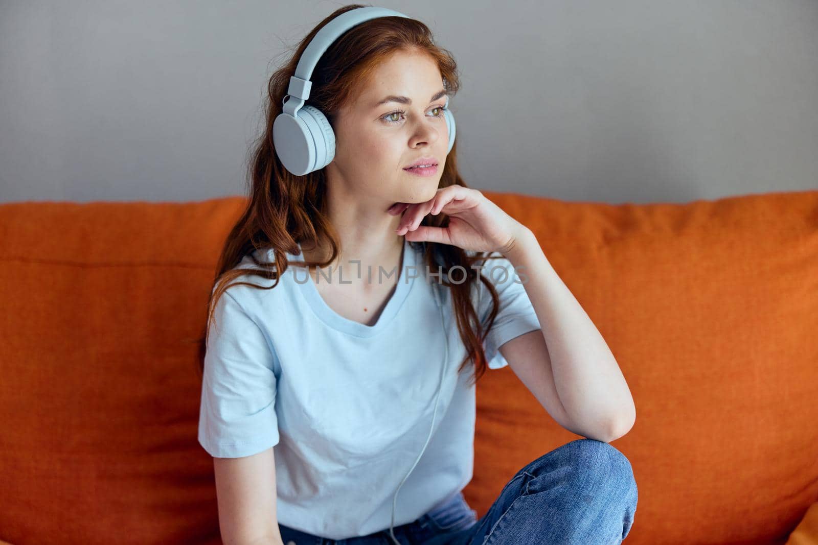 smiling woman sitting on the couch at home listening to music on headphones Lifestyle. High quality photo