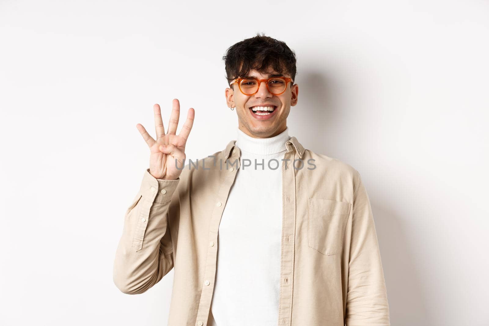 Handsome young man making order, showing number four fingers and smiling, standing on white background.