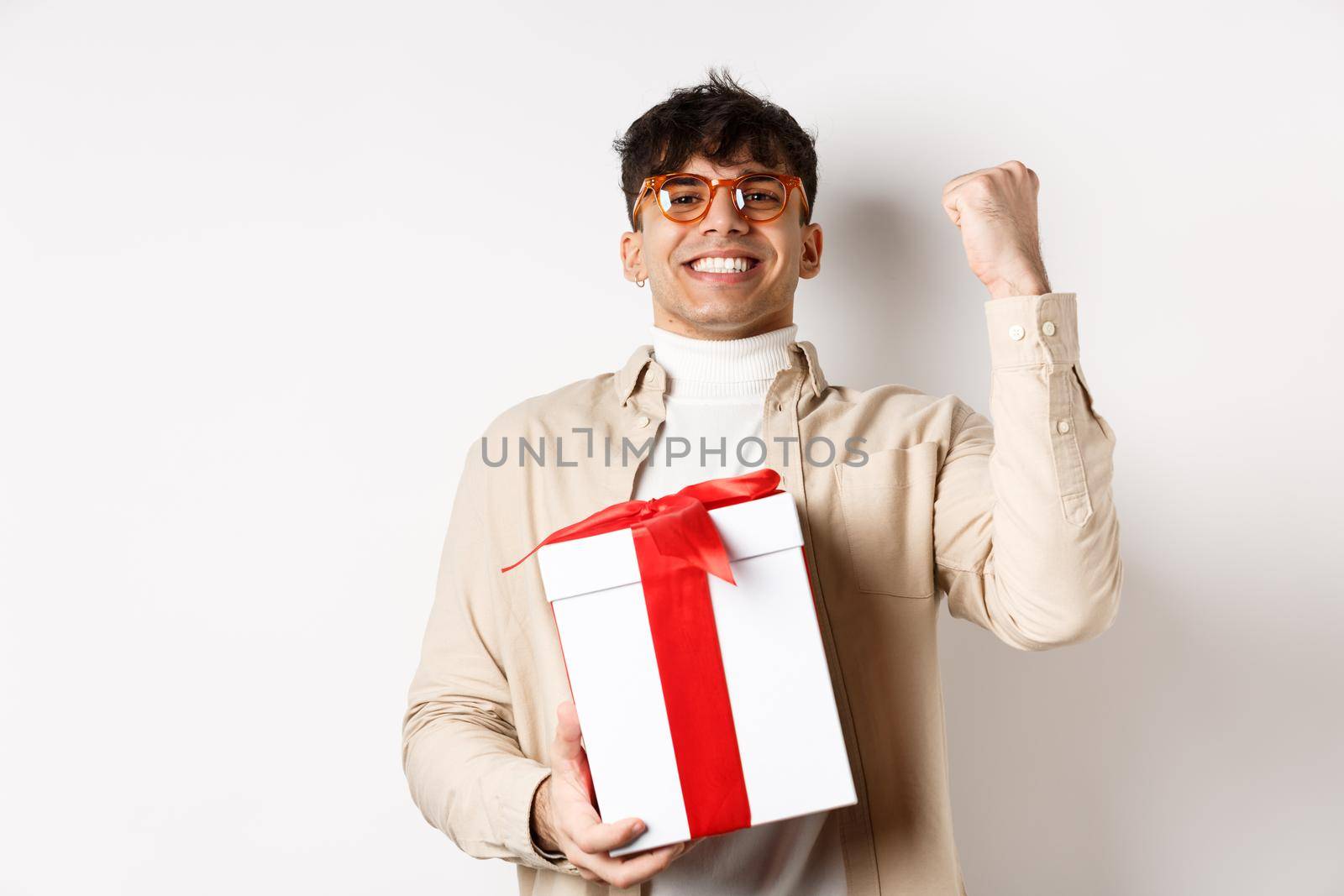 Cheerful guy saying yes as receiving gift, making fist pump and rejoicing, got present, standing on white background.