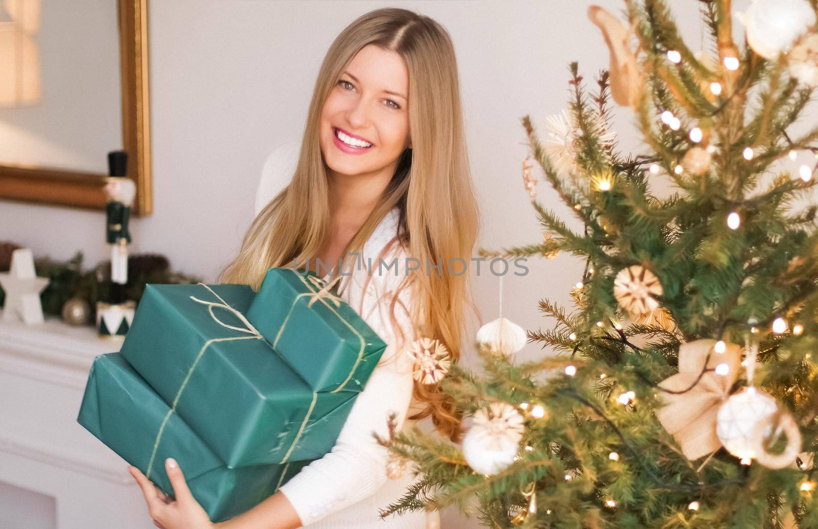 Christmas holiday and gifts for her concept. Happy smiling woman holding wrapped present boxes at home, xmas tree on background.