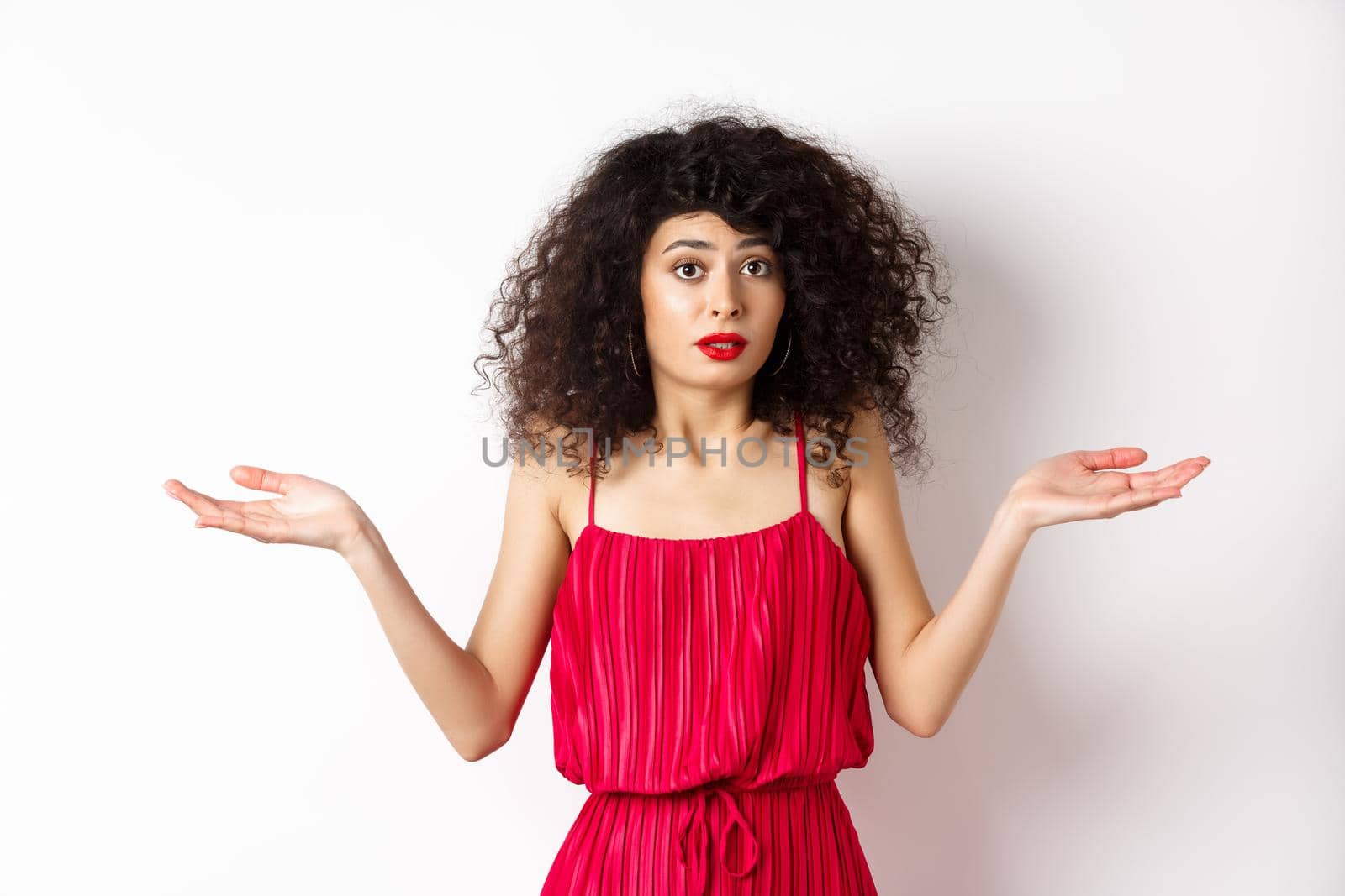 Confused lady in red dress shrugging shoulders, spread hands sideways and looking puzzled, know nothing, cant understand, standing over white background by Benzoix