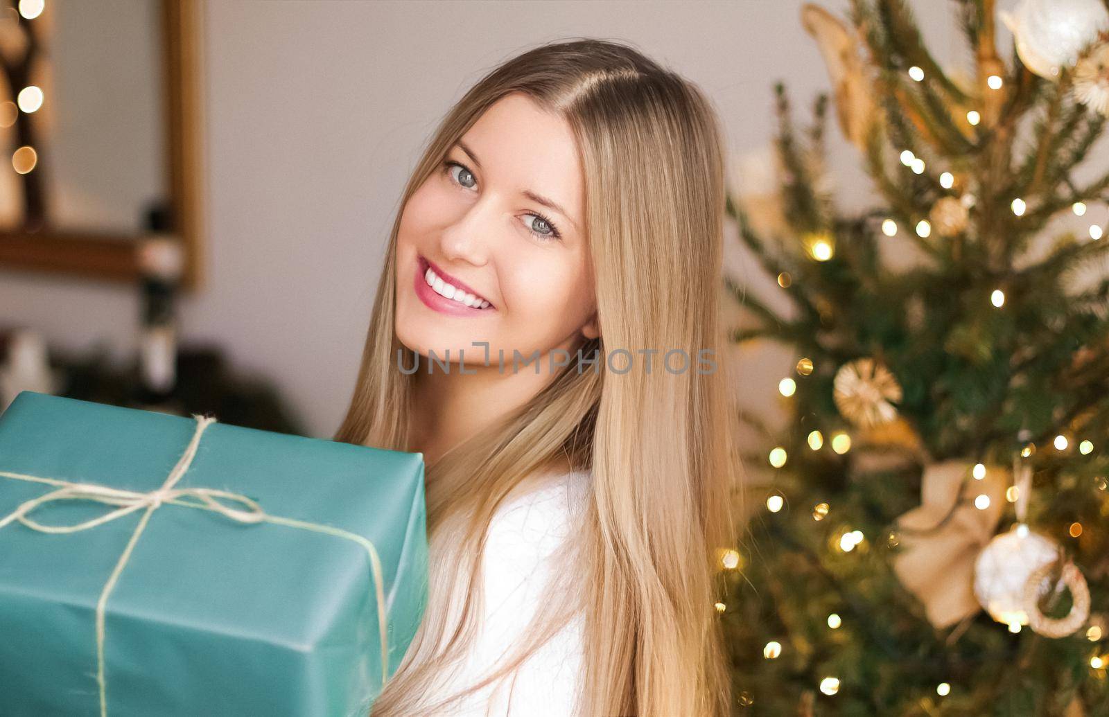 Christmas holiday and gift for her concept. Happy smiling woman holding wrapped present, xmas tree on background.