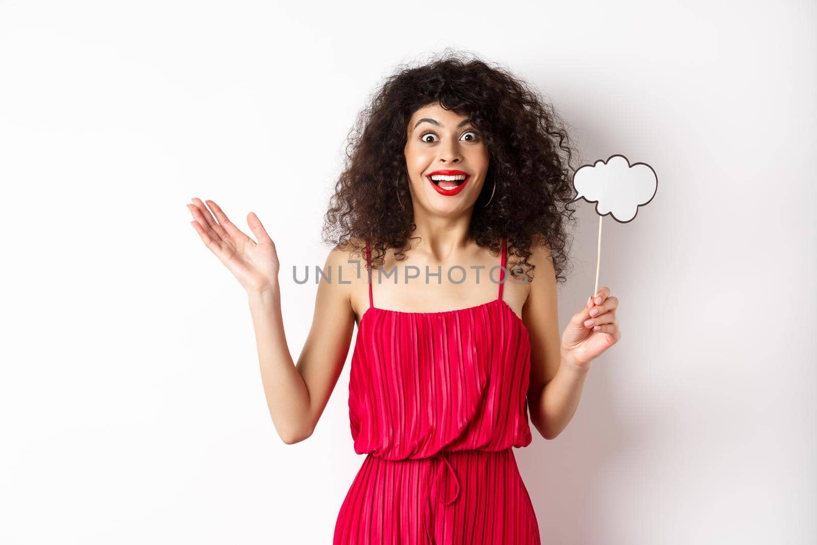 Happy young woman in red dress, holding comment cloud and looking surprised, standing over white background by Benzoix