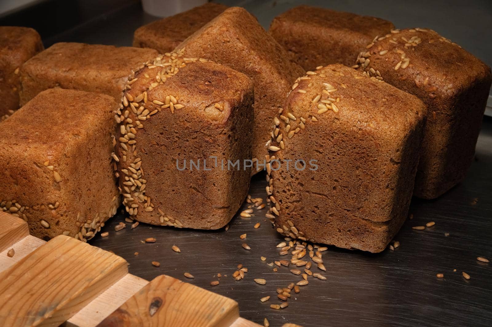A lot of whole delicious homemade rectangular rye bread with sunflower seeds on top lies on a wooden rack background.