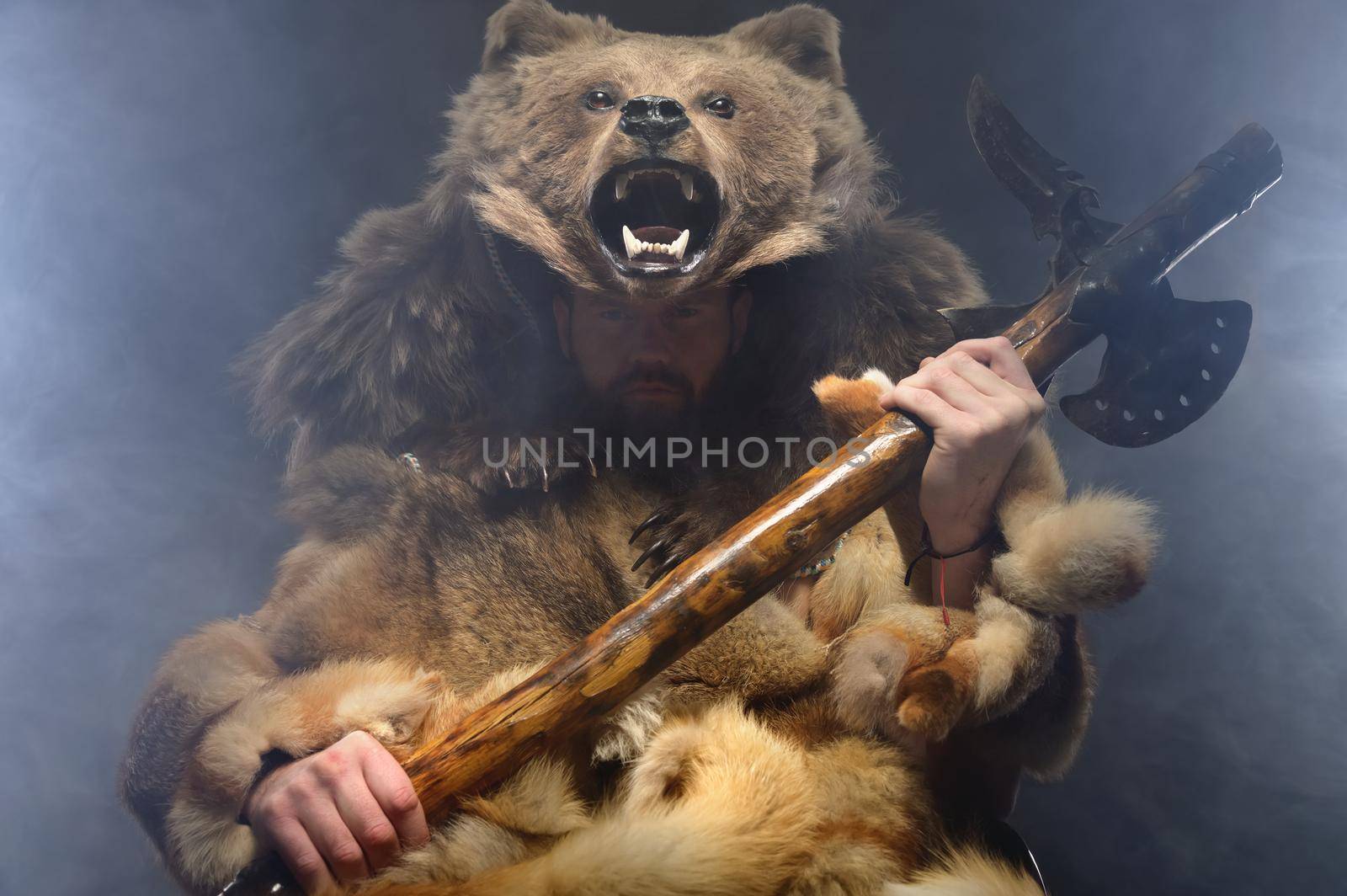 Portrait of a man Bearded Scandinavian shaman with axe on hands and a bear skin on his head. Caucasian man dressed in animal skins pensively looks at camera