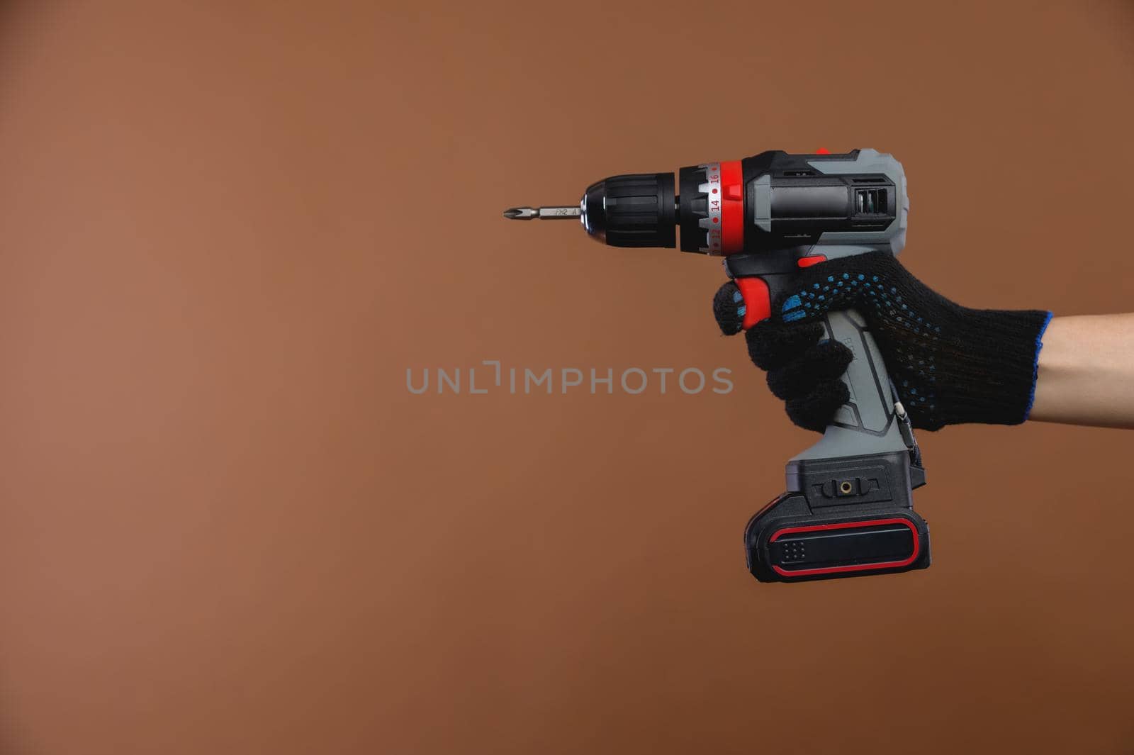 Repair, fix the problem, or tighten the bolt at the construction site. In a female hand a screwdriver or drill, a repair tool, photo on a brown background