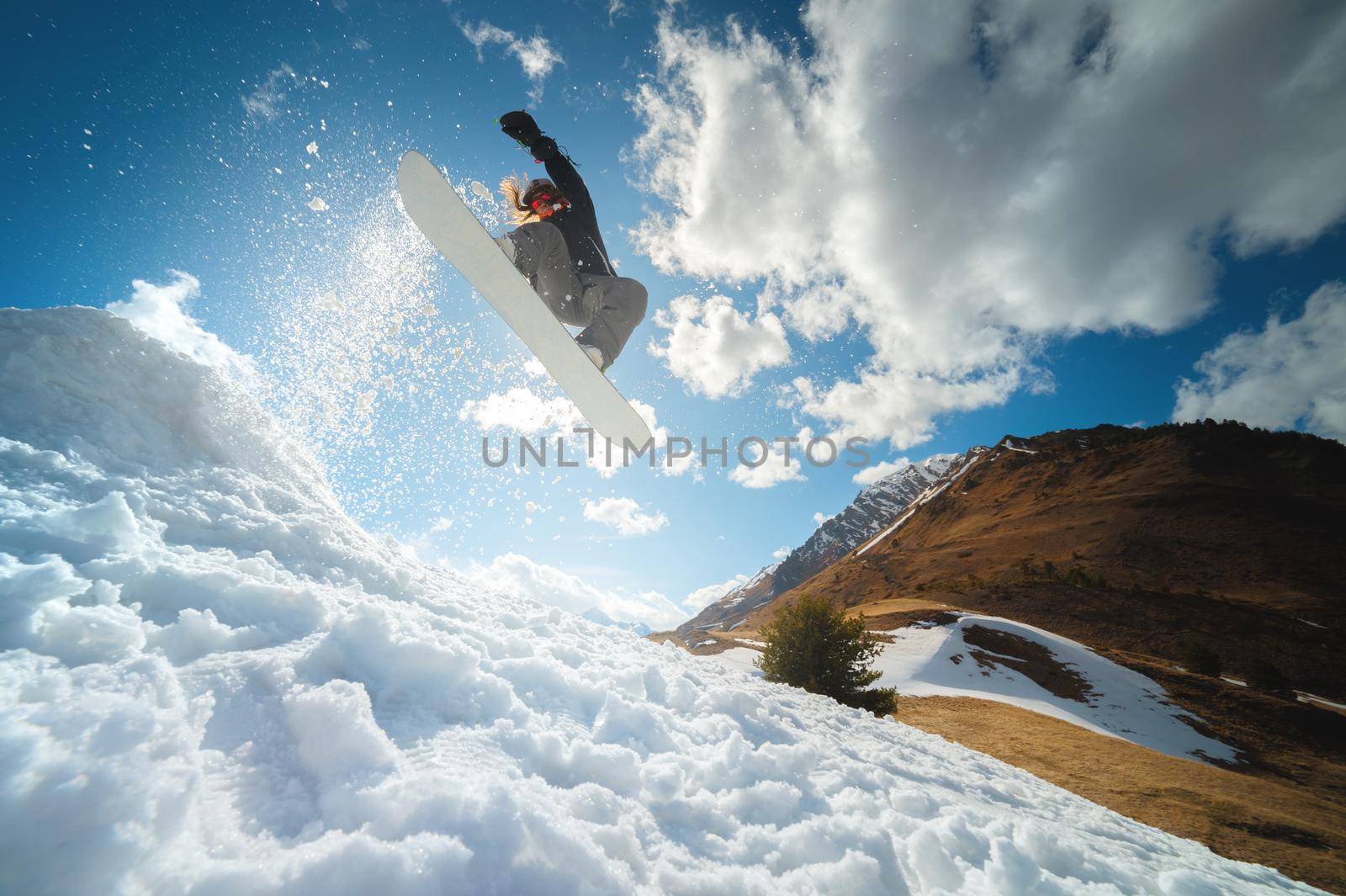 Extreme winter sports. Young professional woman snowboarder rides a halfpipe. Jumps from a halfpipe trampoline in the sun, performs tricks and turns with grabs in a sunny winter.