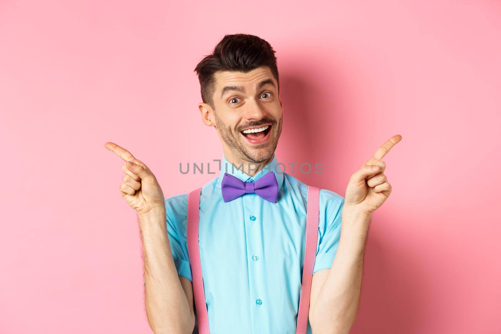 Handsome funny guy pointing fingers aside, showing left and right logo and smiling, recommending two choices, standing on pink background.