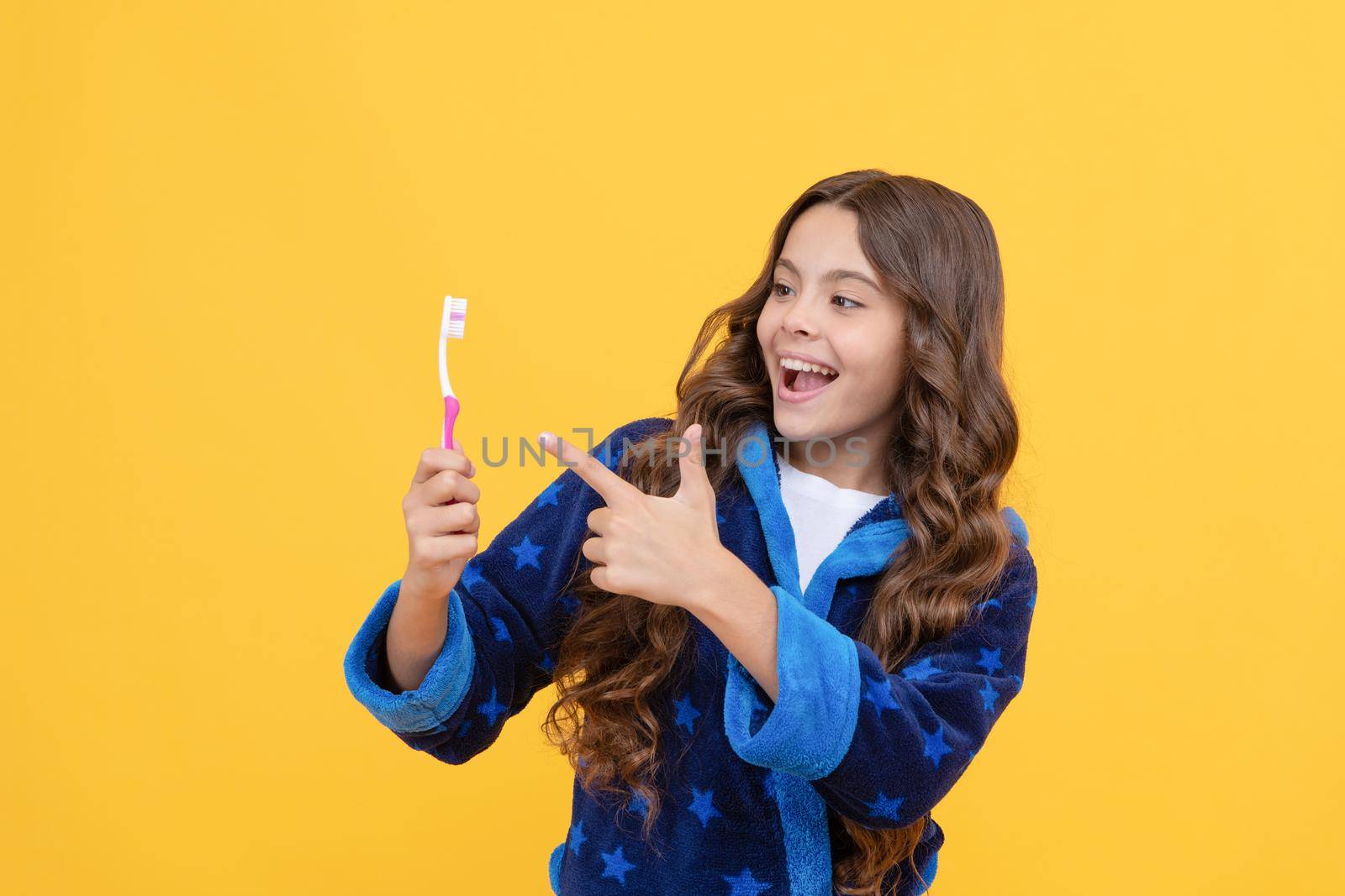 happy child girl in cozy bathrobe pointing finger on toothbrush in morning, dental care.