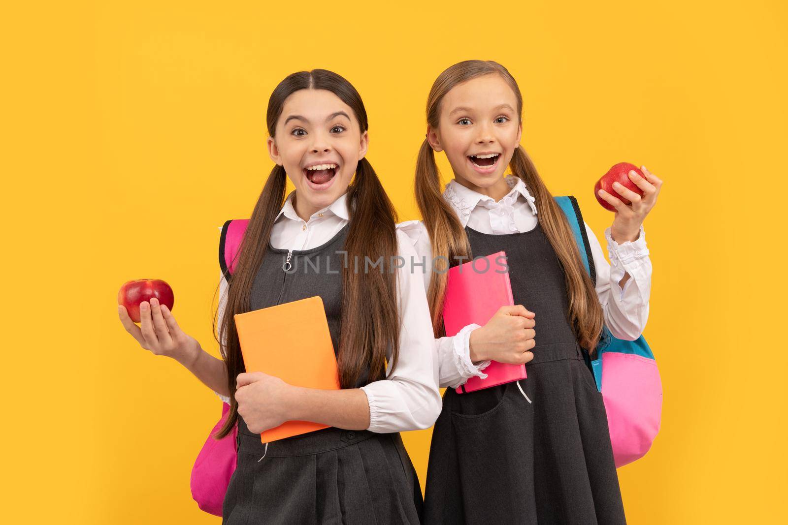 Happy kids in school uniforms hold books and apples for healthy eating school meal, snack by RedFoxStudio