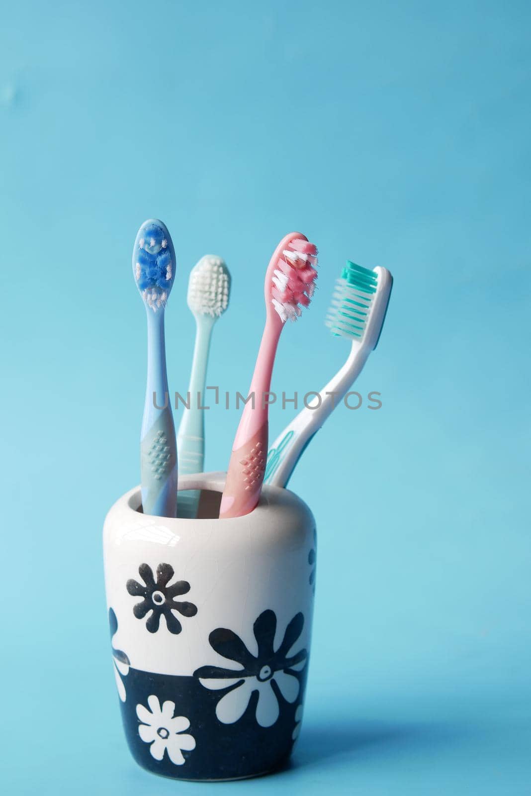 colorful toothbrushes in white mug against blue background by towfiq007