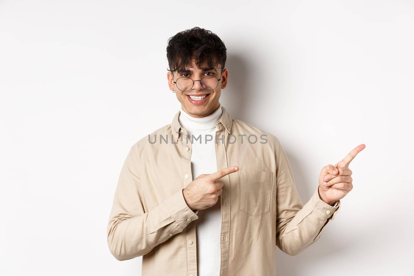 Handsome caucasian man in glasses smiling, pointing fingers at upper right corner, showing logo on white background by Benzoix