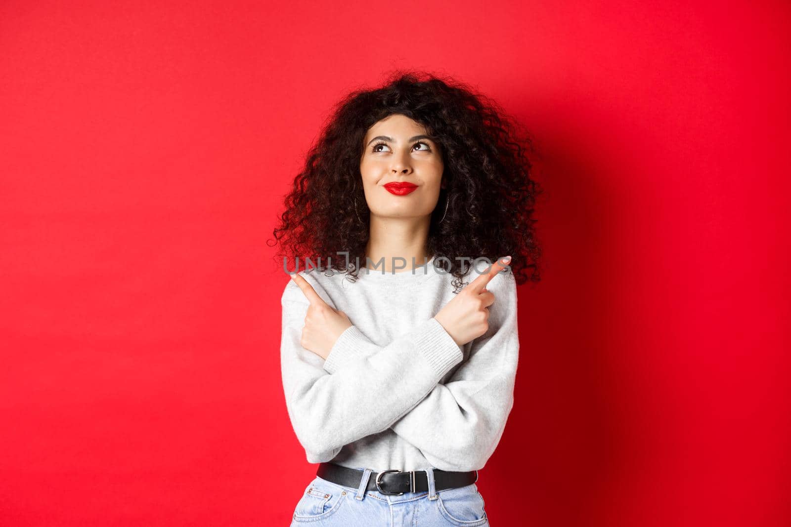 Image of happy smiling woman pointing sideways, looking up with determined face, choose something, standing confident in her decision on red background.