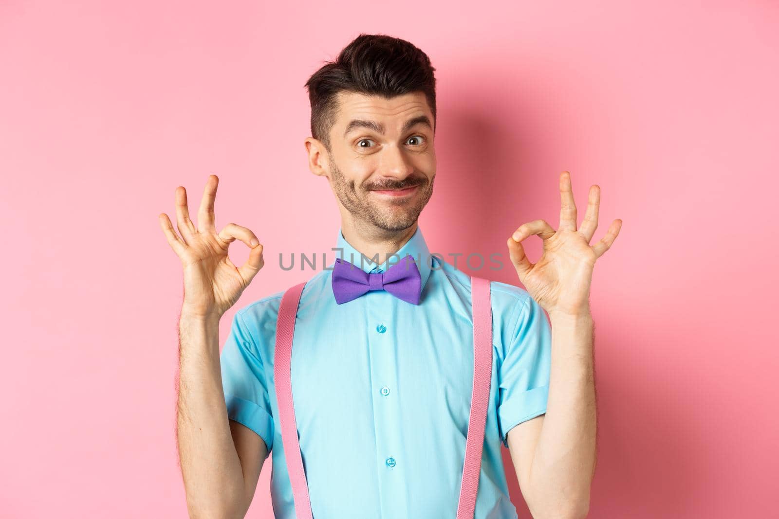 Portrait of handsome man with moustache and bow-tie, showing okay gestures and smiling in approval, recommending good offer, standing over pink background by Benzoix