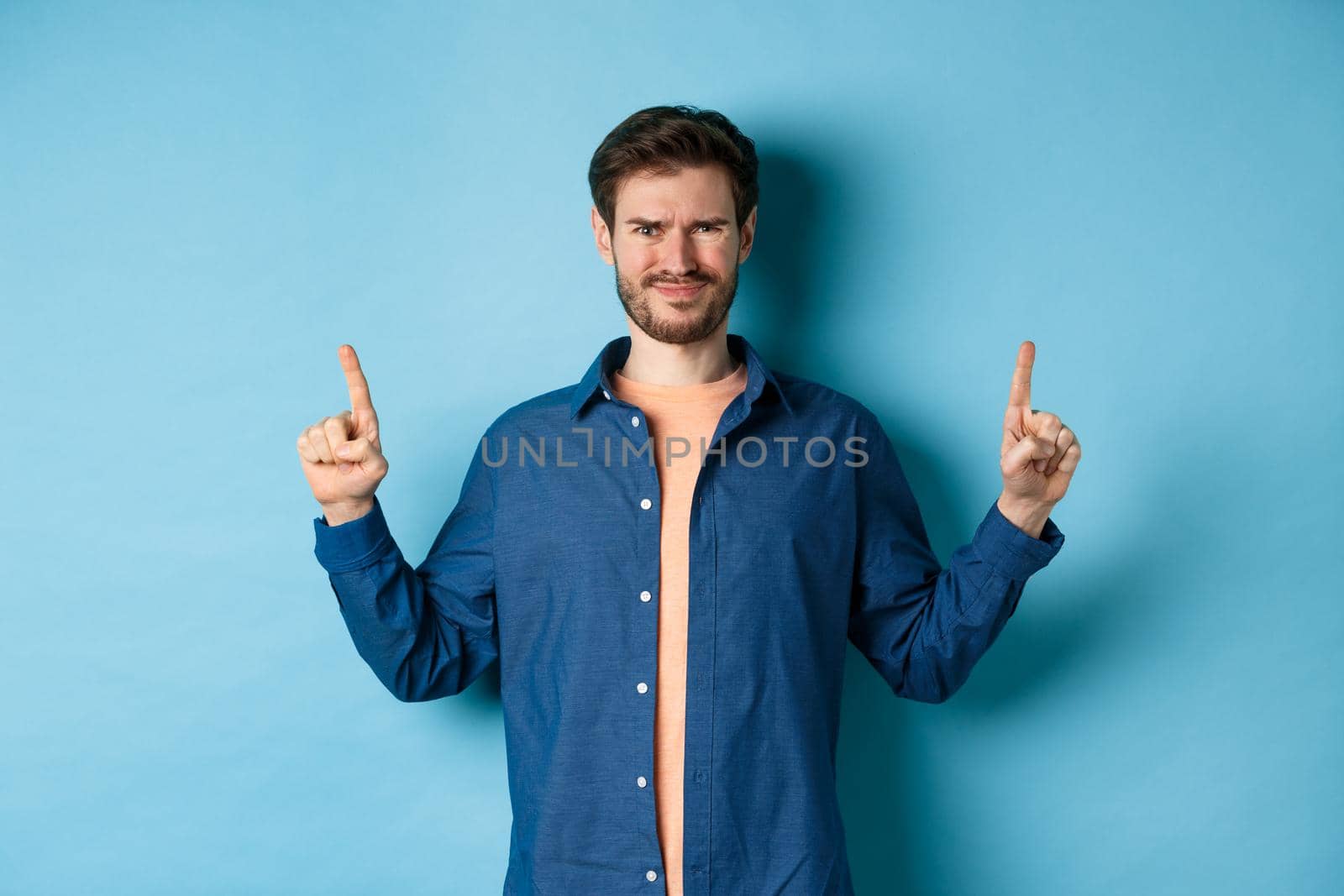 Skeptical young man frowning and squinting, cringe from something disgusting, standing on blue background.