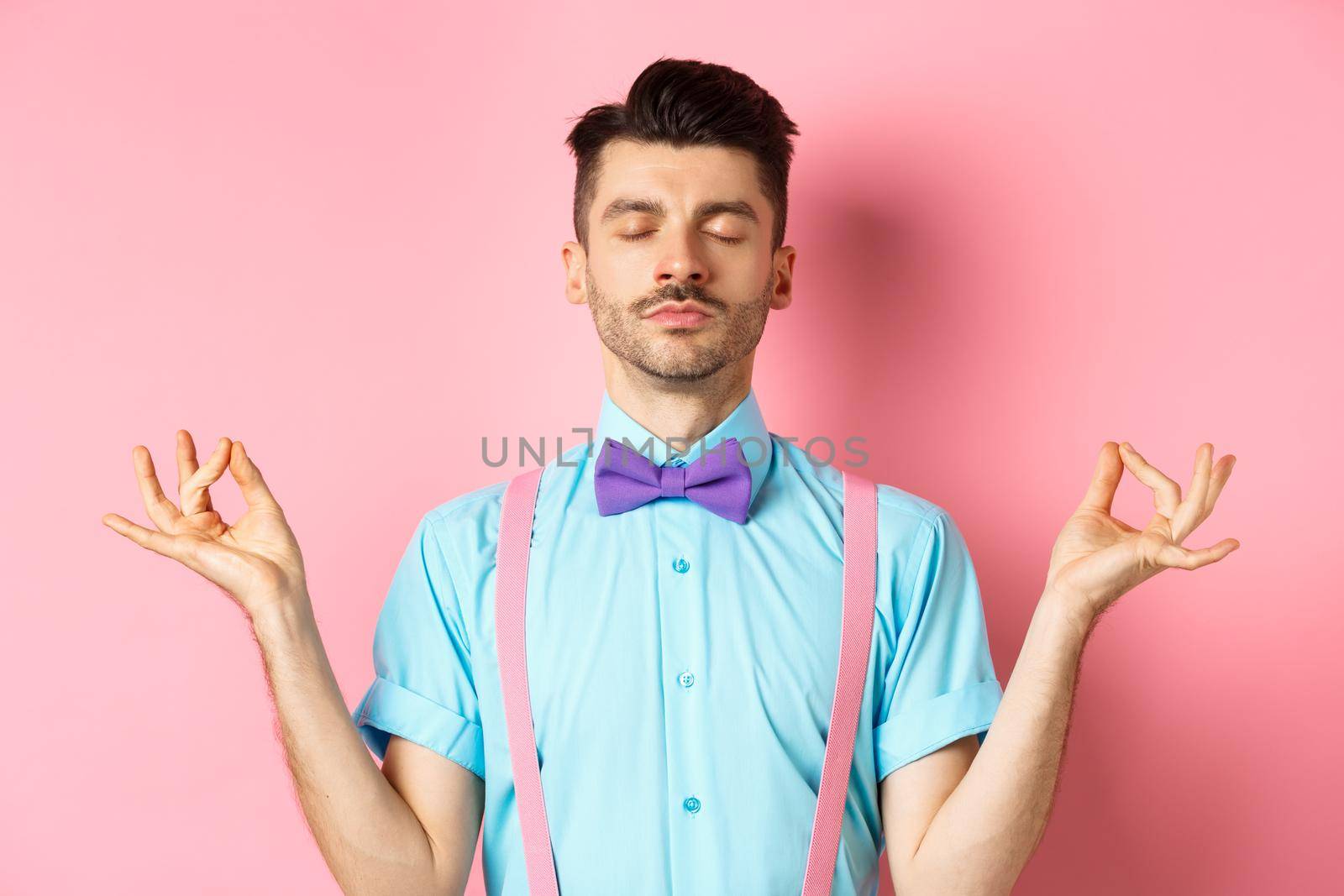 Young guy in bow-tie standing calm and peaceful, meditating with hands in mudra zen gesture and closed eyes, practice yoga to relax, standing over pink background.