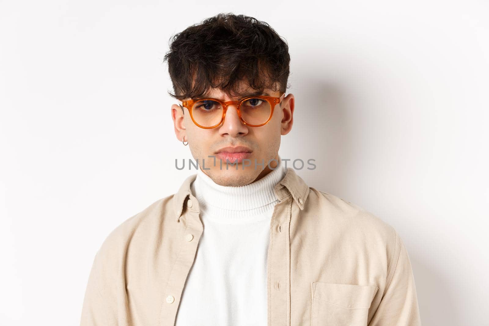 Close up portrait of angry frowning guy looking with dispise, standing mad on white background, wearing glasses.