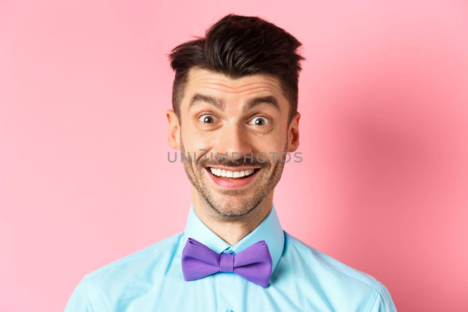 Close-up of cheerful caucasian man smiling happy, looking at something interesting, standing in bow-tie over pink background by Benzoix