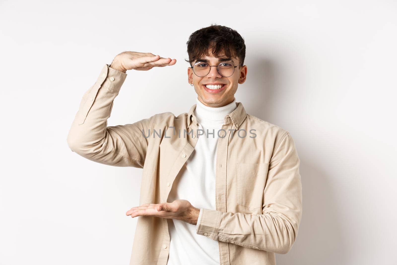 Real people. Happy modern guy in glasses showing big size, shaping box and smiling, showing something large, standing on white background.