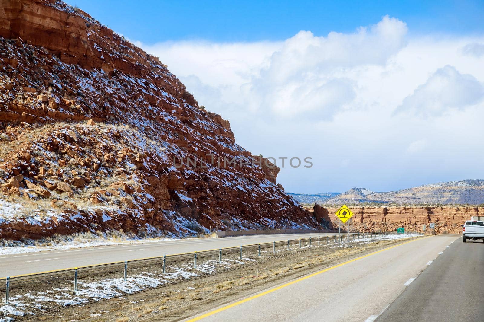 The snow-covered red rock mountain range behind desert landscape along I-40 highway in New Mexico by ungvar