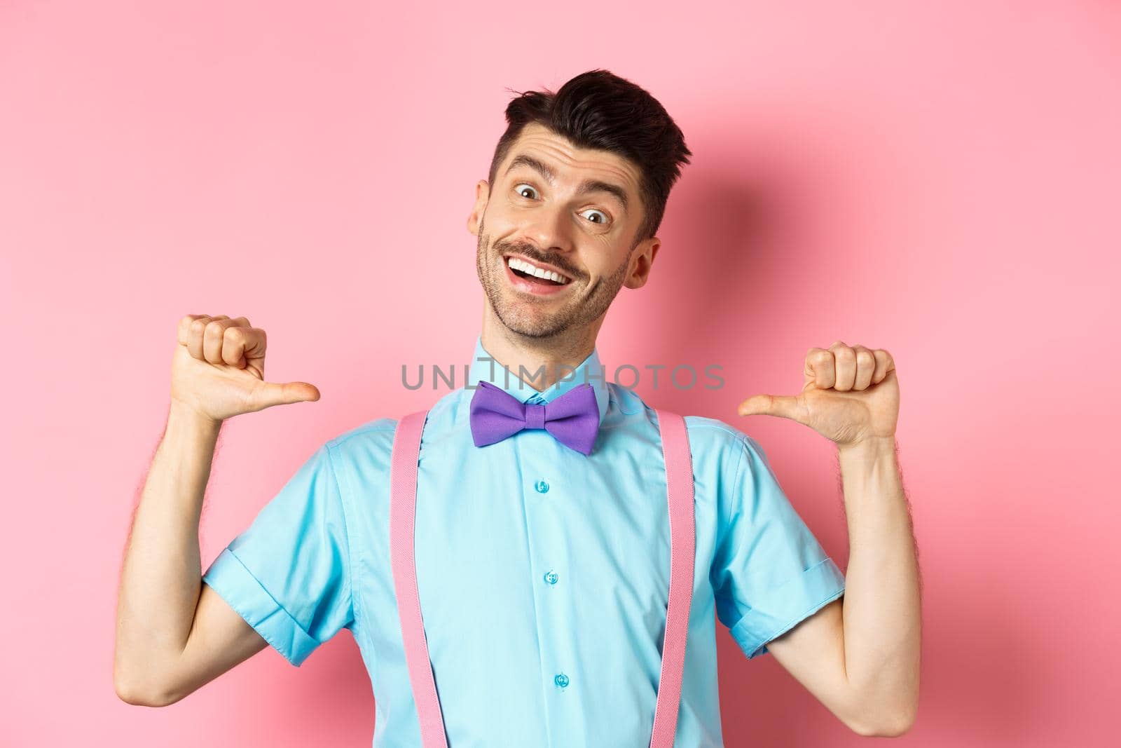 Cheerful smiling man with moustache and bow-tie, pointing at himself and self-promoting, standing happy over pink background in suspenders by Benzoix