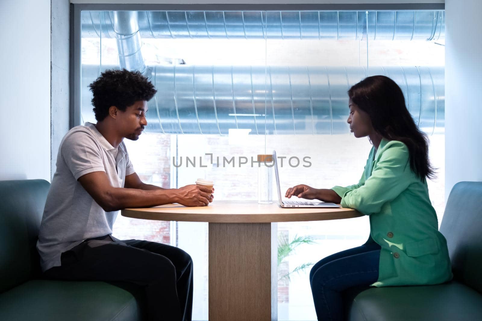 Coworking space. Young african american coworkers share table to work using laptop. by Hoverstock