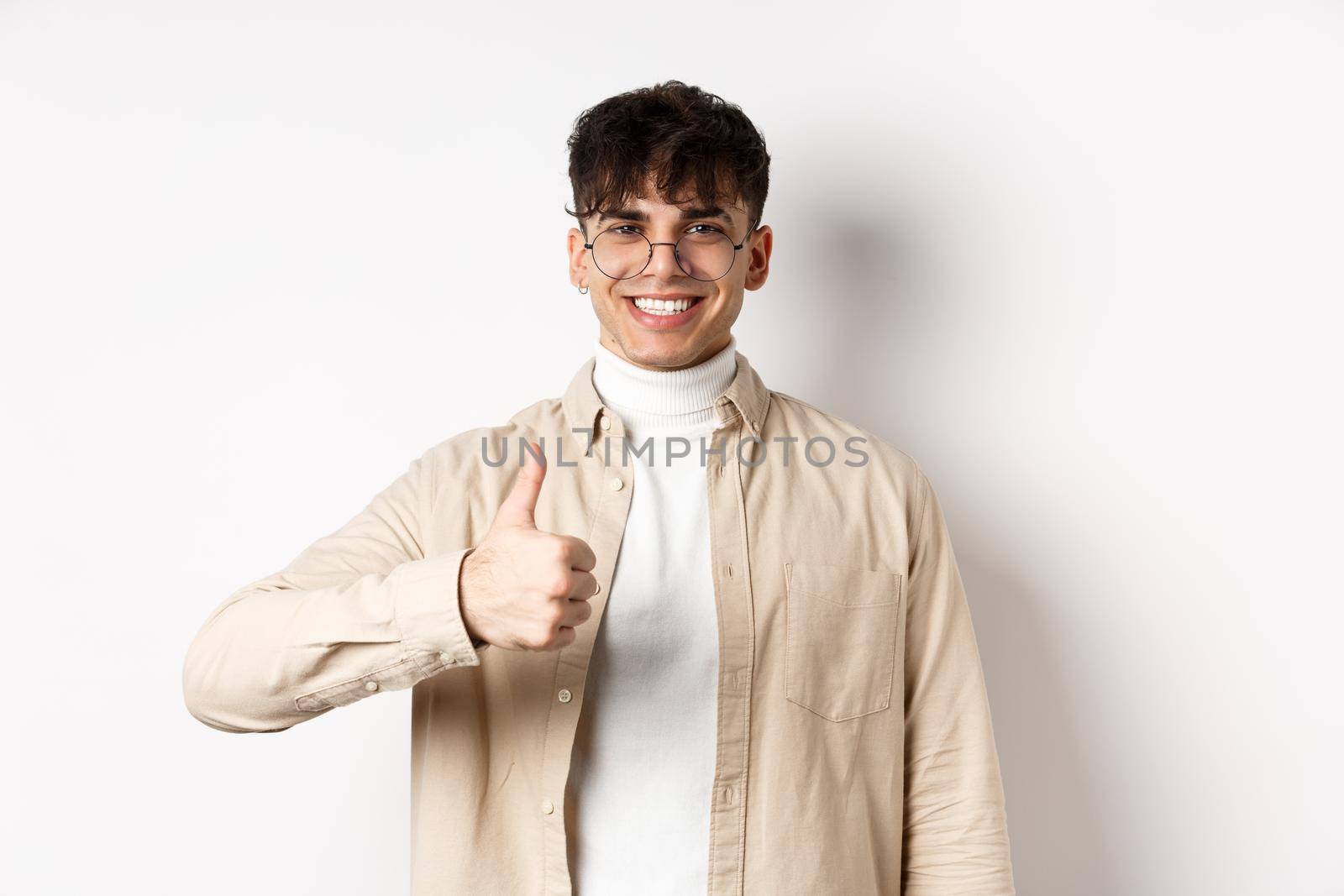 Positive smiling man showing thumbs up and looking satisfied, recommending and approving thing, standing pleased on white background by Benzoix