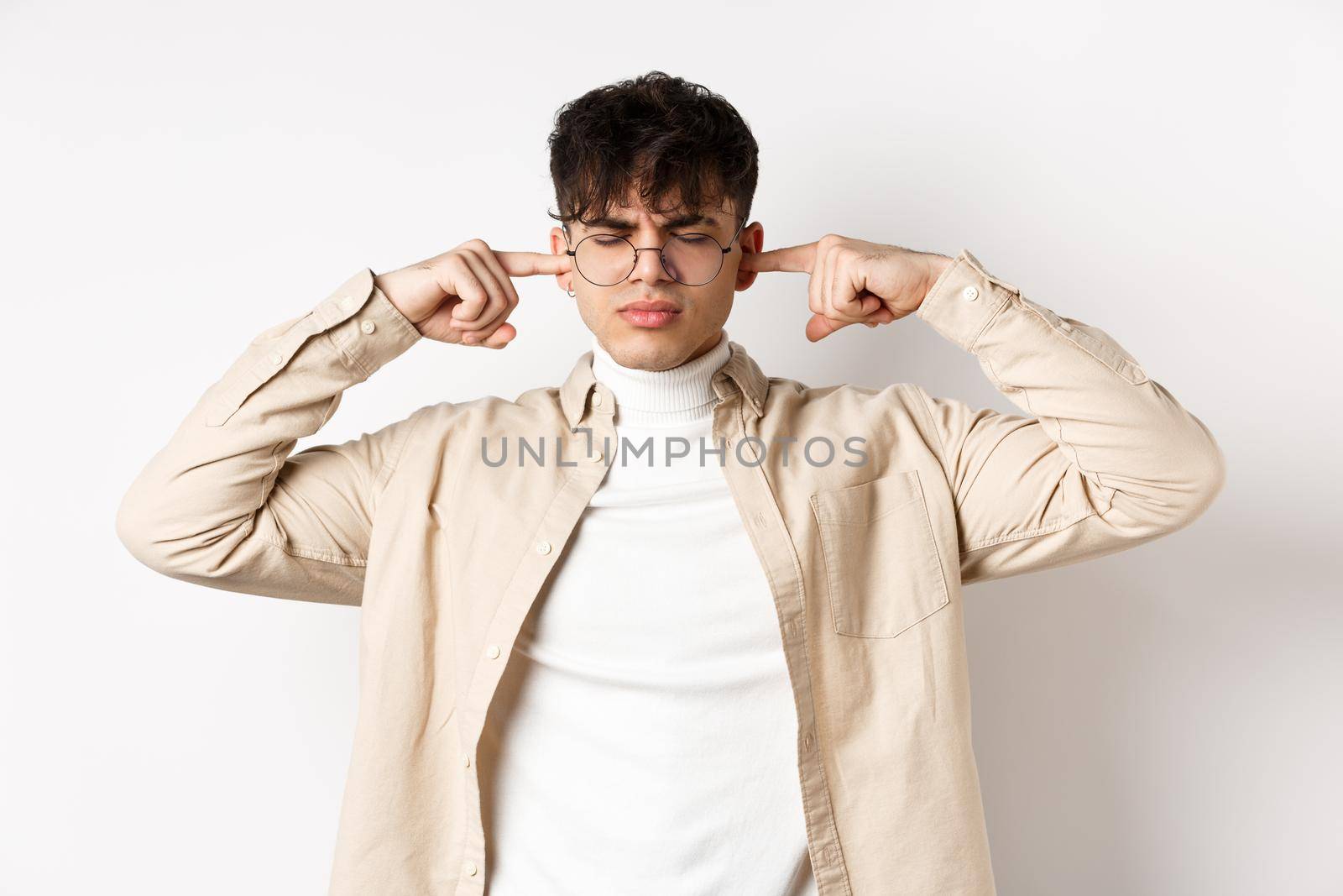 Annoyed young man shut his ears, block annoying sound, unwilling to listen, standing on white background by Benzoix