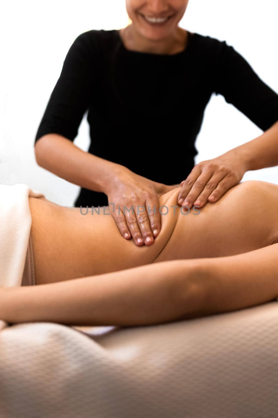 Happy masseuse working on female client mid back enjoying her job. Woman receiving massage relaxing in spa. by Hoverstock