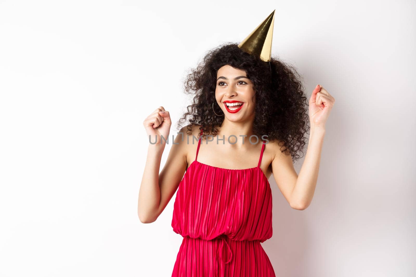 Happy birthday girl celebrating, wearing party hat and red dress, dancing and having fun, standing against white background.