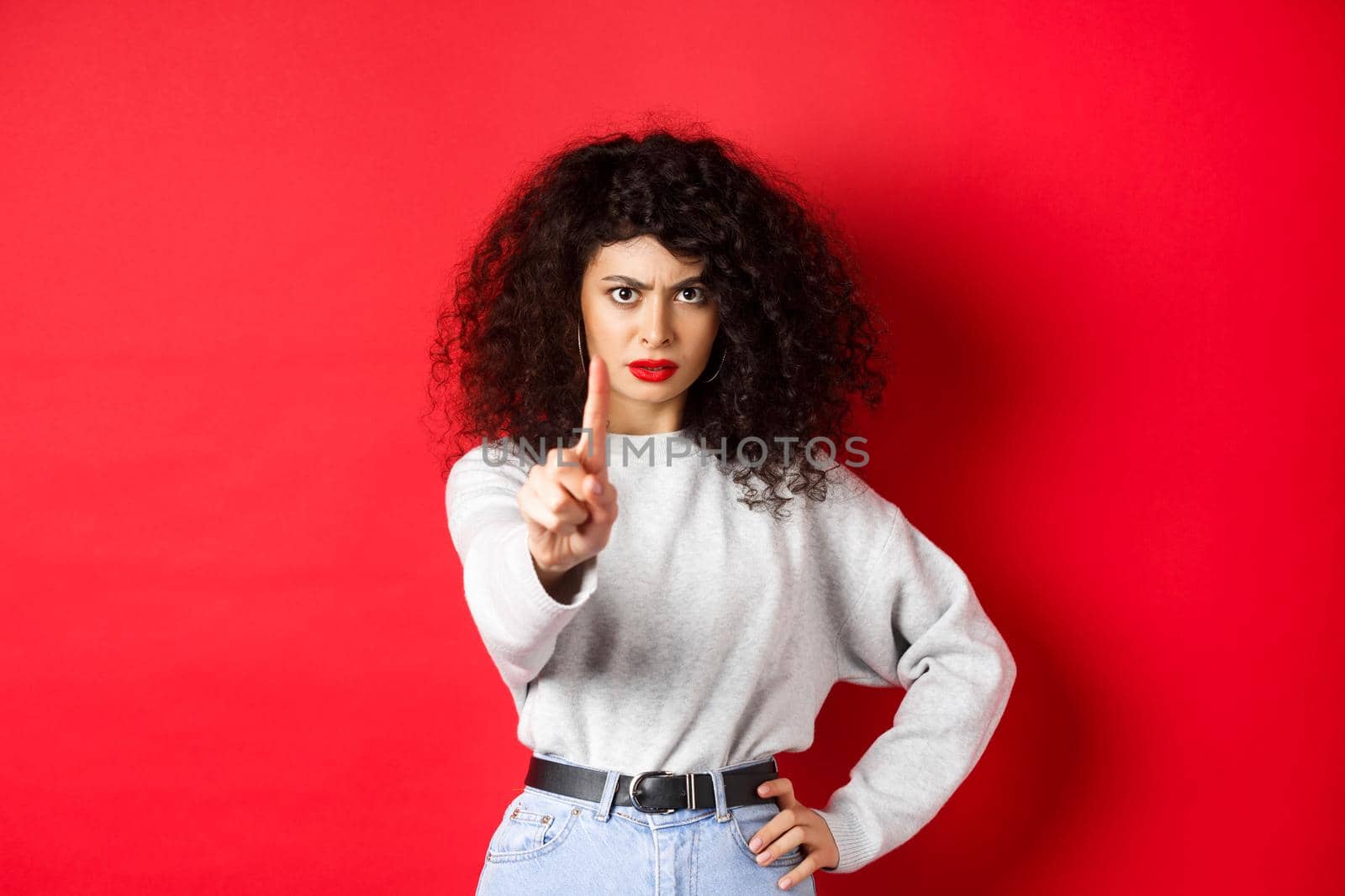 Serious confident woman say no, extend one finger to stop you, prohibit something bad, standing determined against red background.