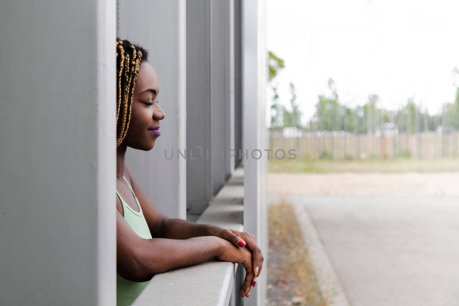 Relaxed and calm young african american woman with long blond braids leans on balcony with eyes closed. Copy space.