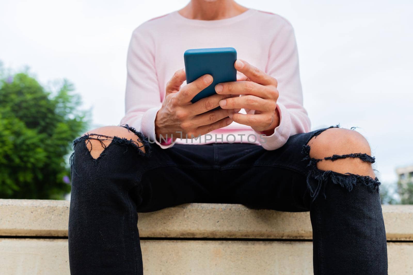 Unrecognisable caucasian man with pink sweater holding cellphone reading text messages. Using mobile phone apps. by Hoverstock
