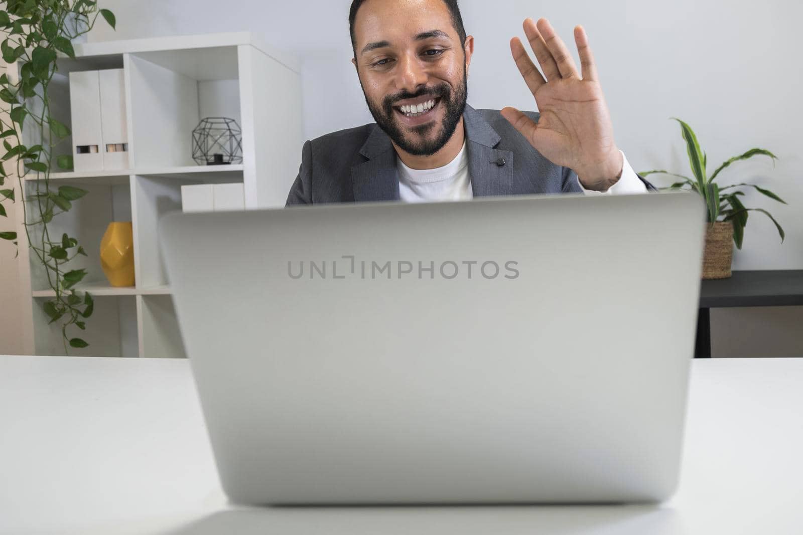 African american businessman on business videocall waves his hand using laptop. by Hoverstock