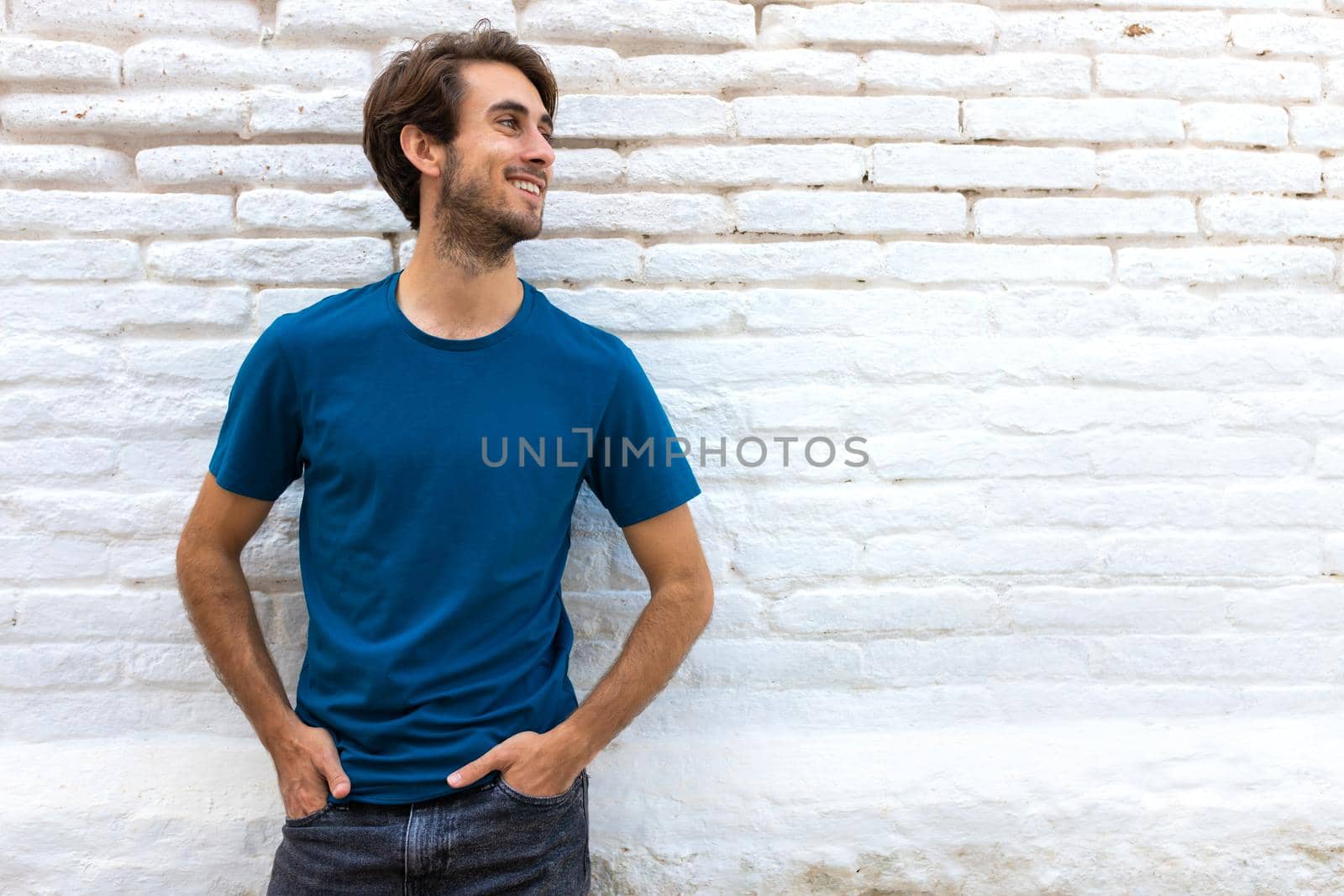 Smiling confident young caucasian man standing next to white brick wall. Copy space. Lifestyle concept.