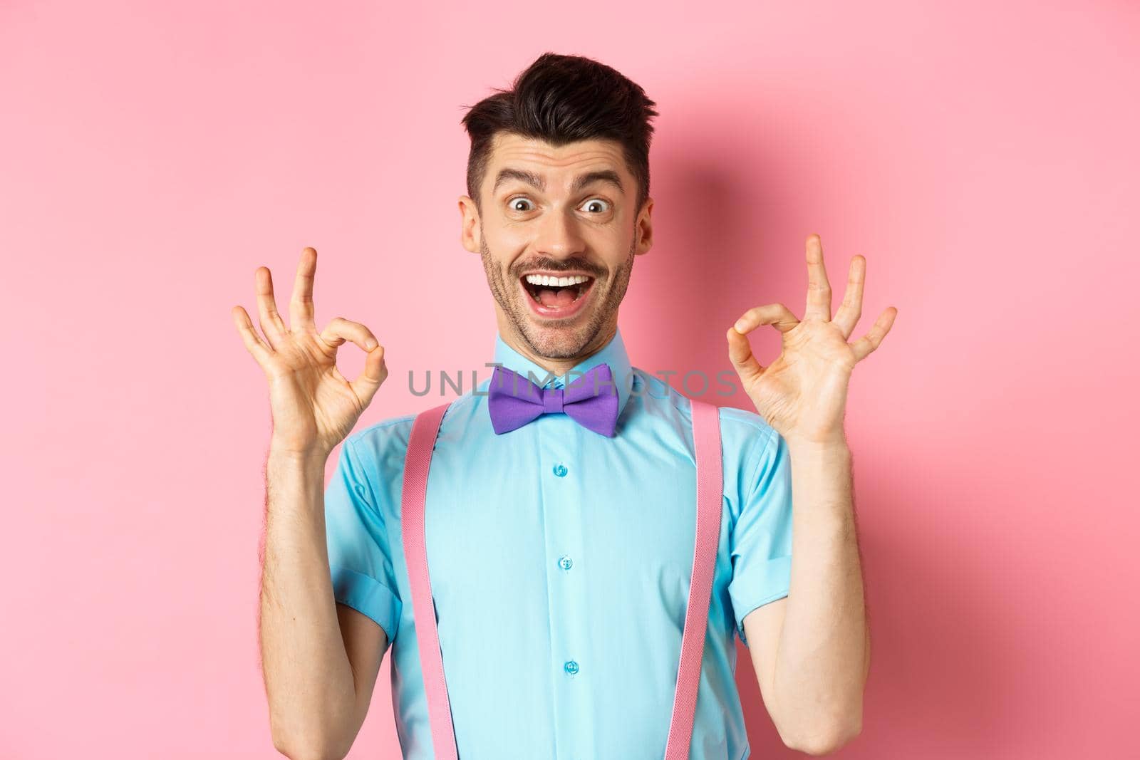 Amazed caucasian guy showing okay gestures and smiling, recommending cool thing, praising awesome offer, standing in pink background.