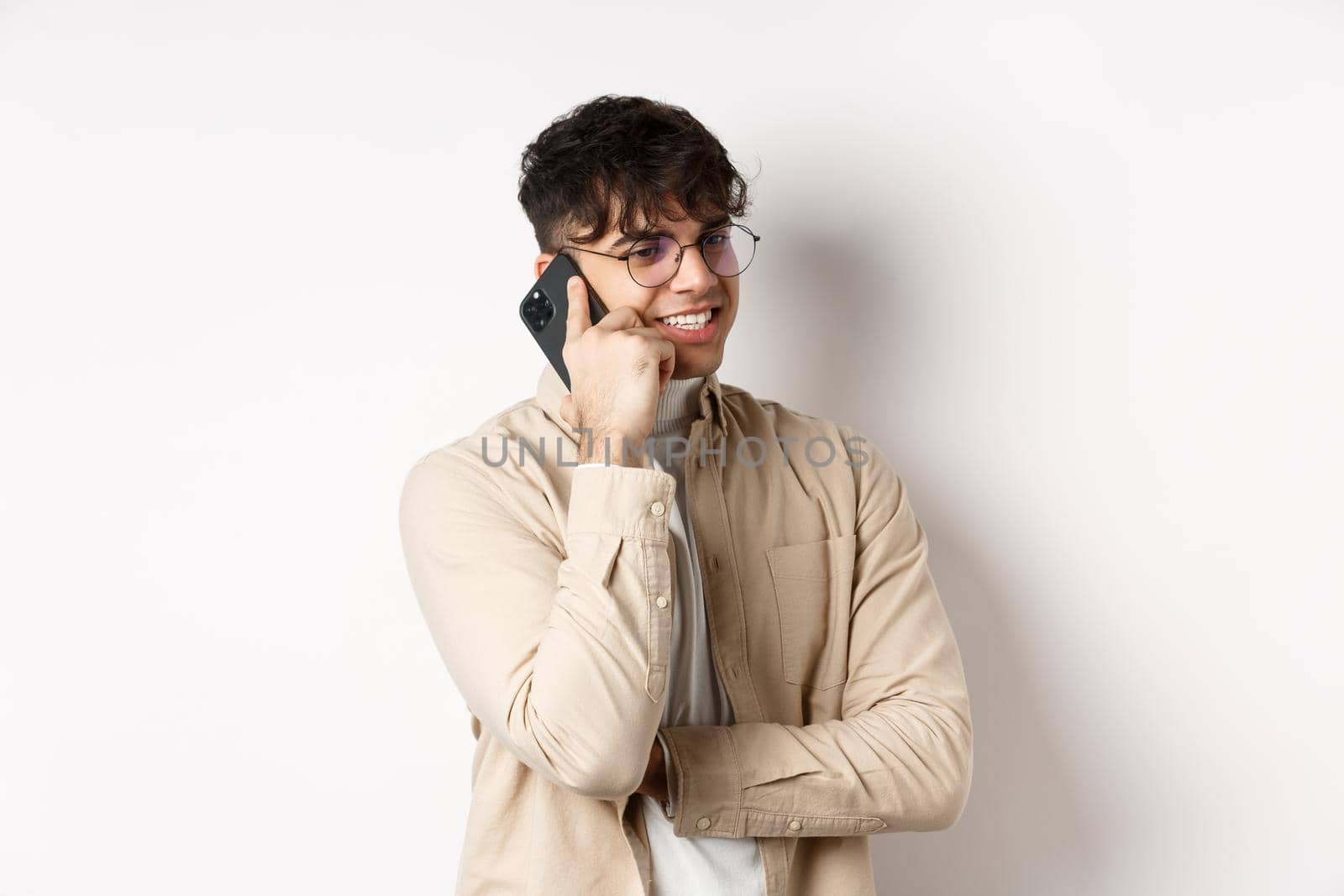 Real people concept. Handsome modern man talking on mobile phone, look aside and holding smartphone near ear, standing on white background.