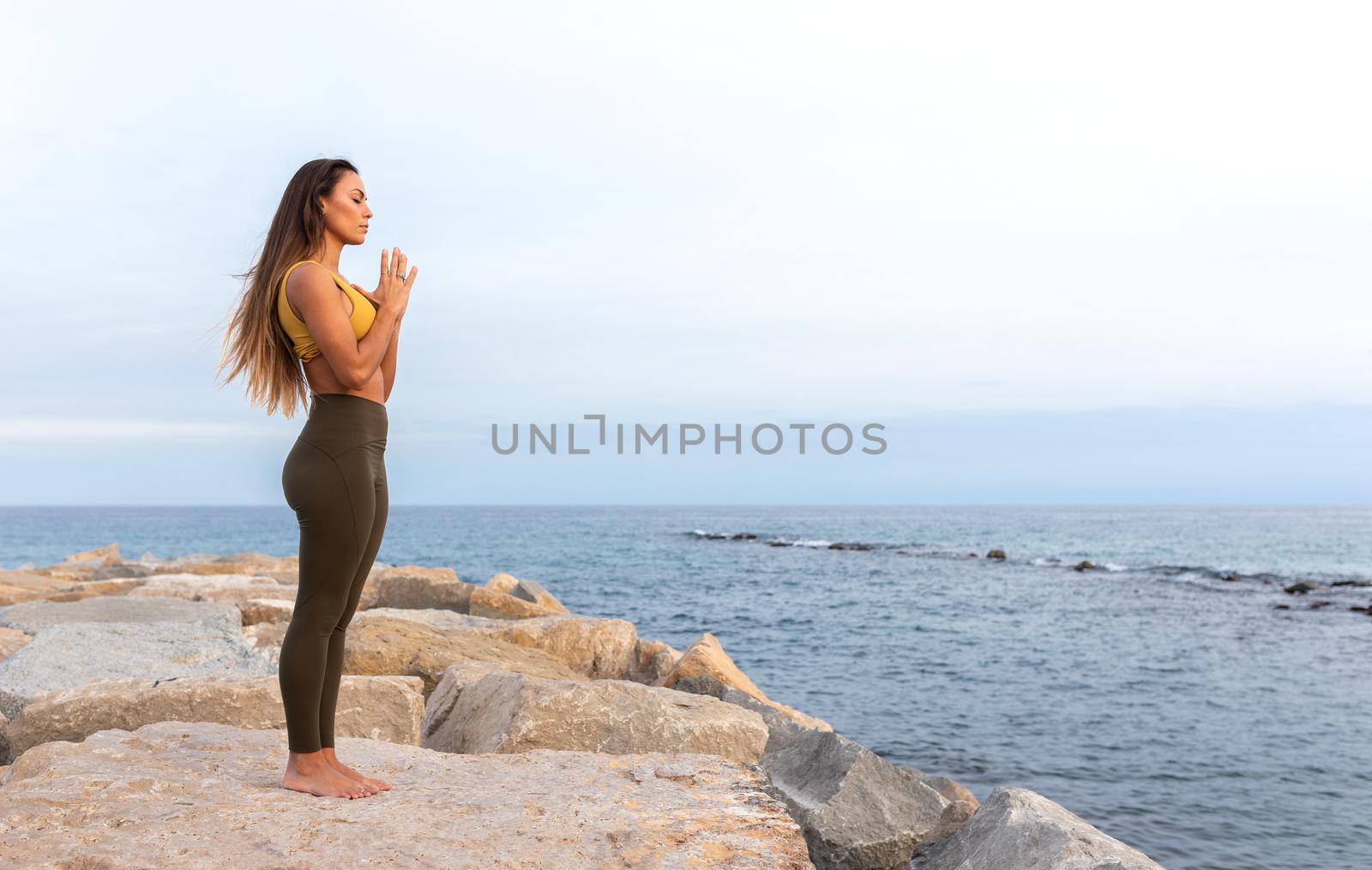 Peaceful young woman standing by the sea with hands in prayer. Copy space. Spirituality and meditation concept.