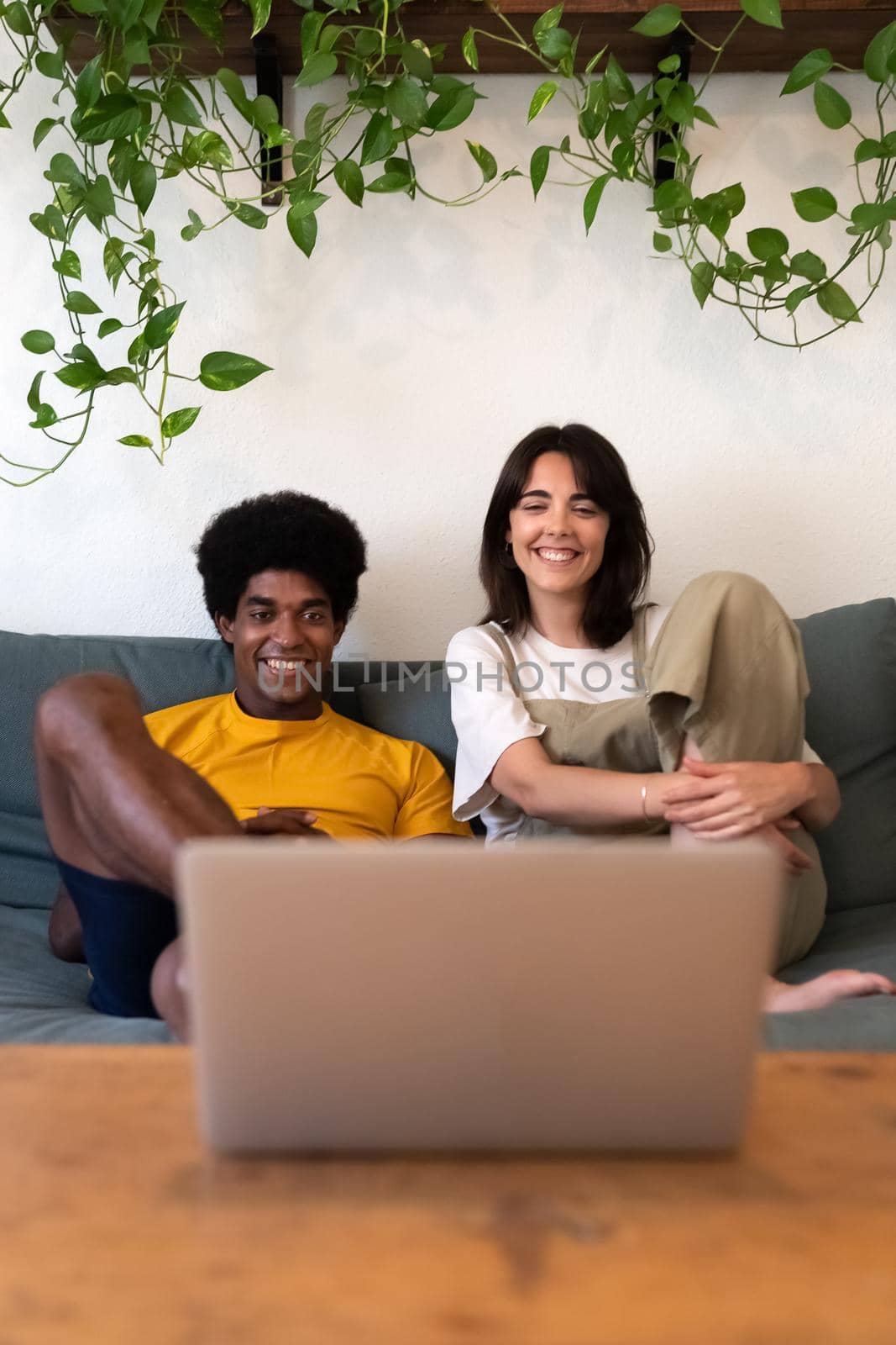 Happy young multiracial couple watching movie on laptop together at home. Vertical image. Lifestyle concept.