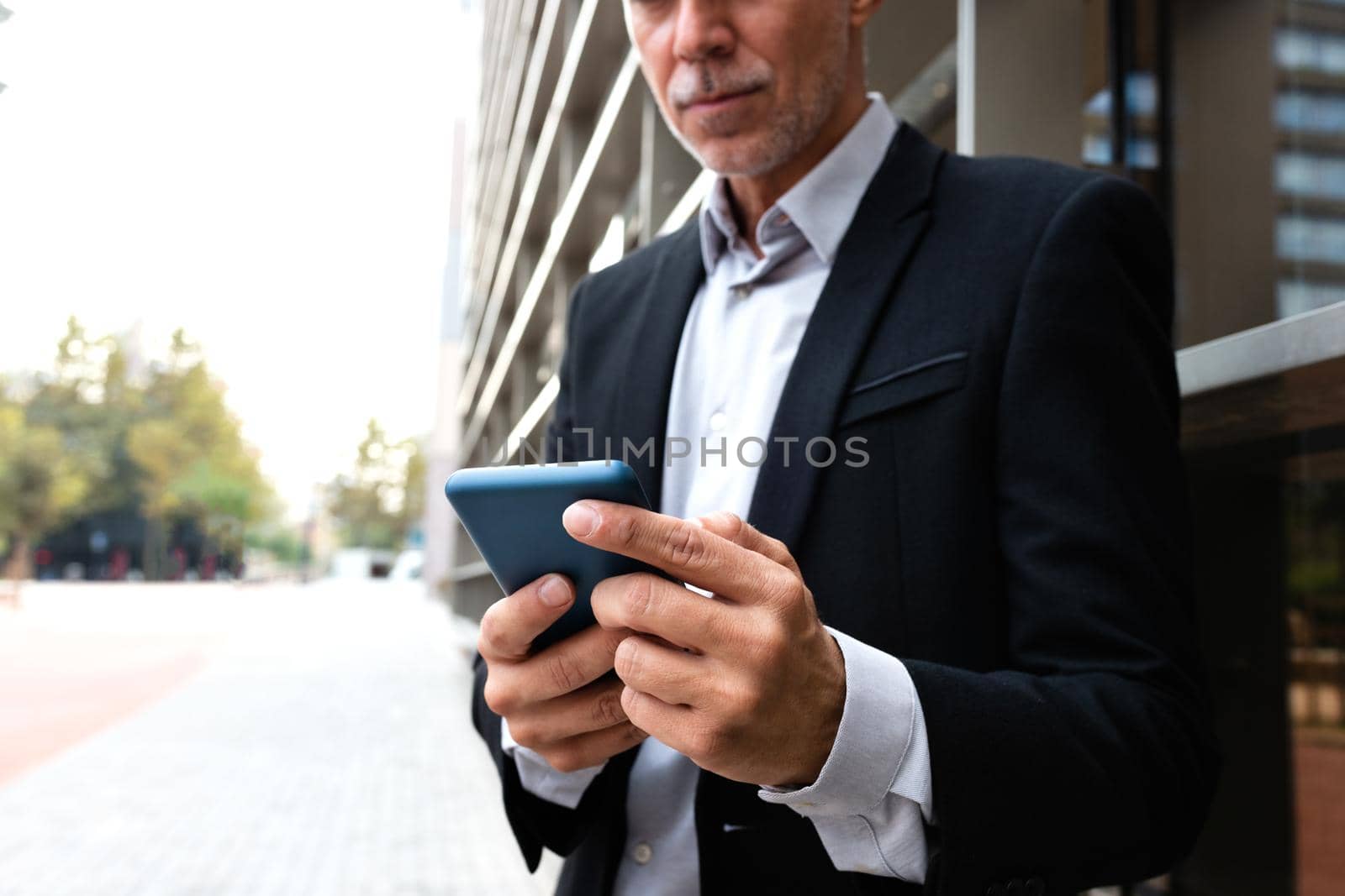 Unrecognizable caucasian man using mobile phone outside the office. Copy space. Selective focus on hands. Business and technology concept.