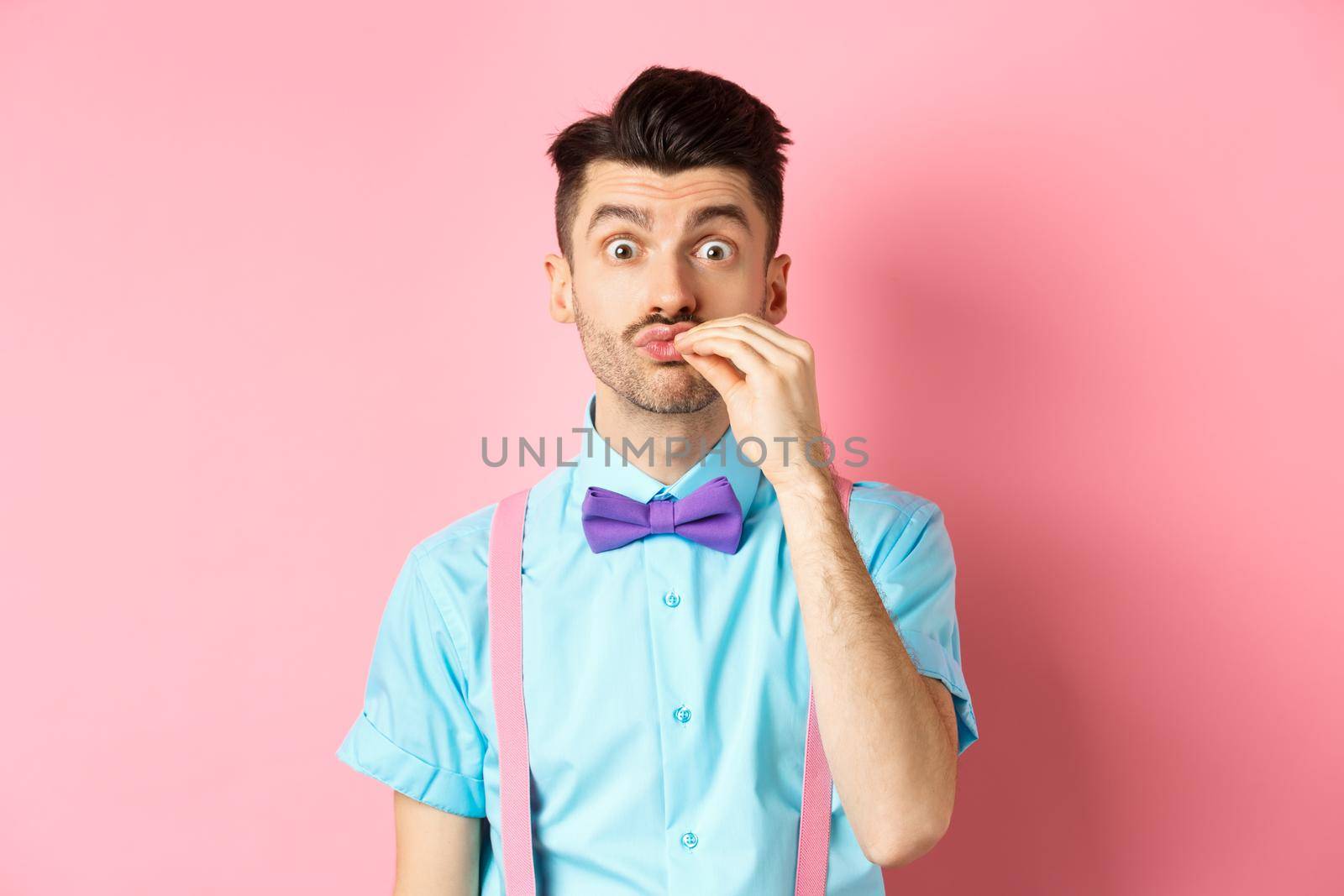 Image of funny guy with moustache and bow-tie showing chefs kiss gesture, compliment excellent product, praising food, standing over pink background.