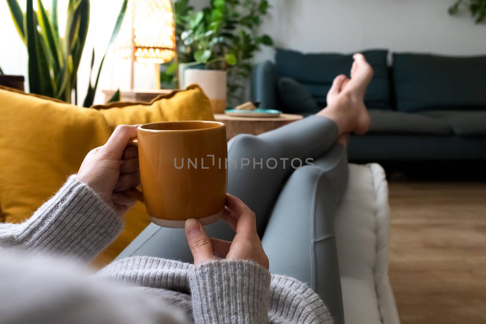 POV of young woman relaxing at home with cup of coffee lying on couch. Lifestyle concept.