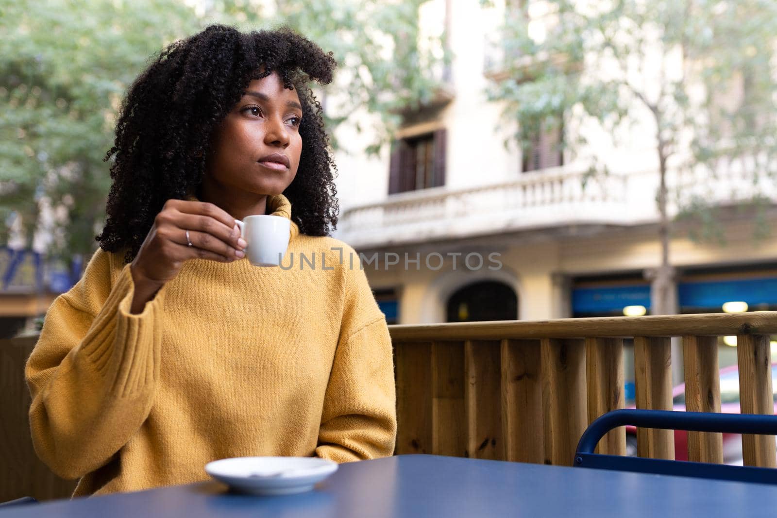 Young African American woman holding coffee cup in outdoors cafe terrace. Copy space. by Hoverstock