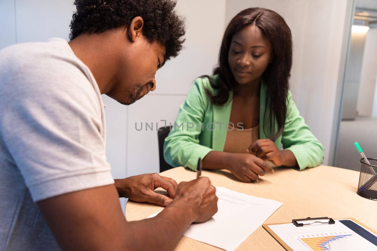 Young African American man signing contract in the office. by Hoverstock