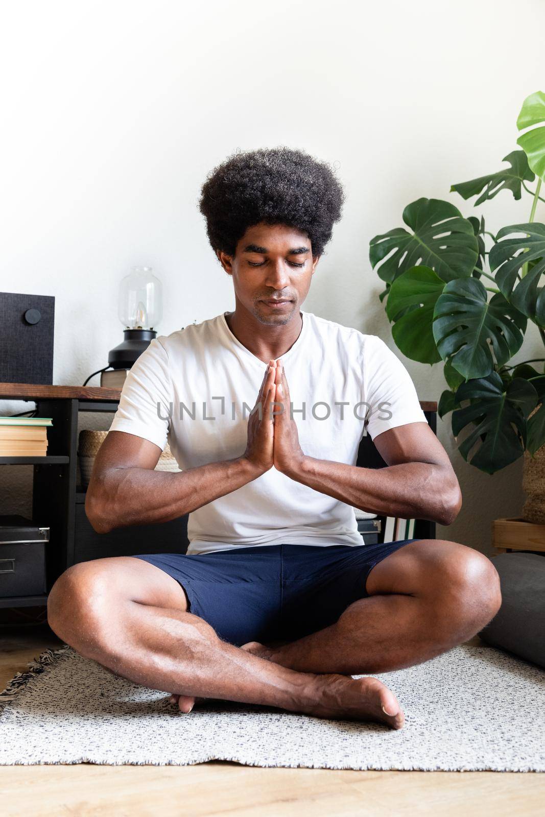Young adult african american man with hands in prayer meditating at home. Vertical image. Meditation concept.