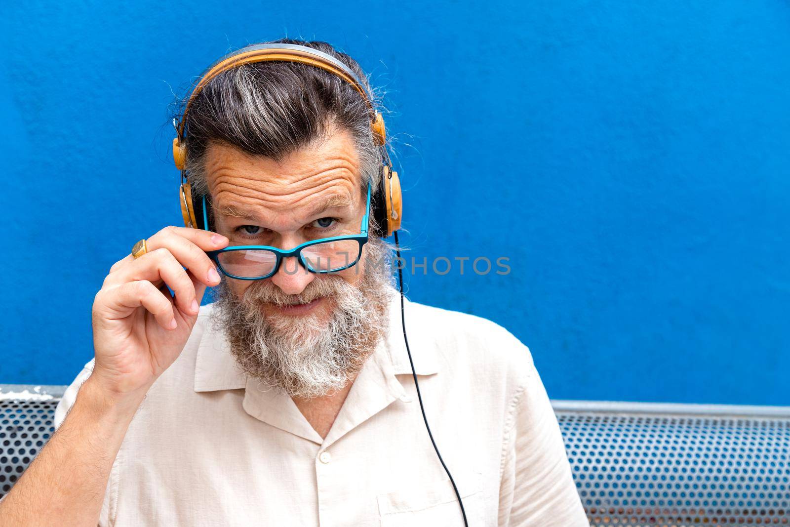 Mature man with headphones wearing eyeglasses looking at camera. Copy space. by Hoverstock
