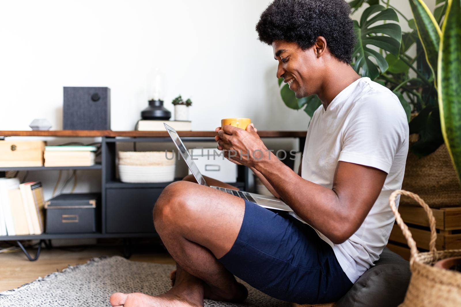 Happy and smiling young african american man has morning coffee while using laptop at home. Copy space. At home concept. Technology concept.
